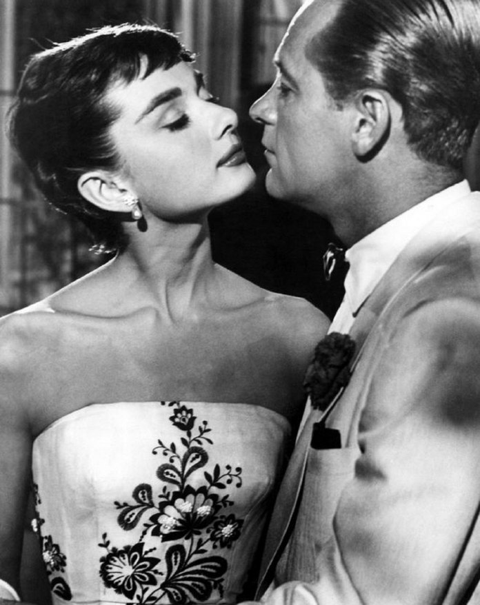 gray scale photo of audrey hepburn and william holden seeing each other